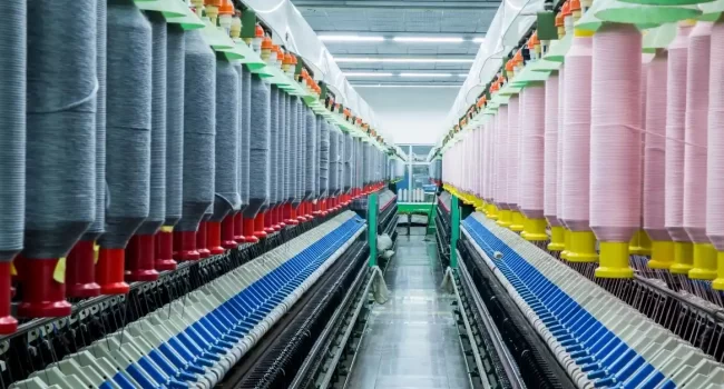 A textile production line featuring rows of yarn spools in various colors, set in a well-lit factory with precision machinery.