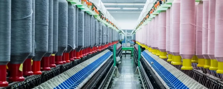 A textile production line featuring rows of yarn spools in various colors, set in a well-lit factory with precision machinery.