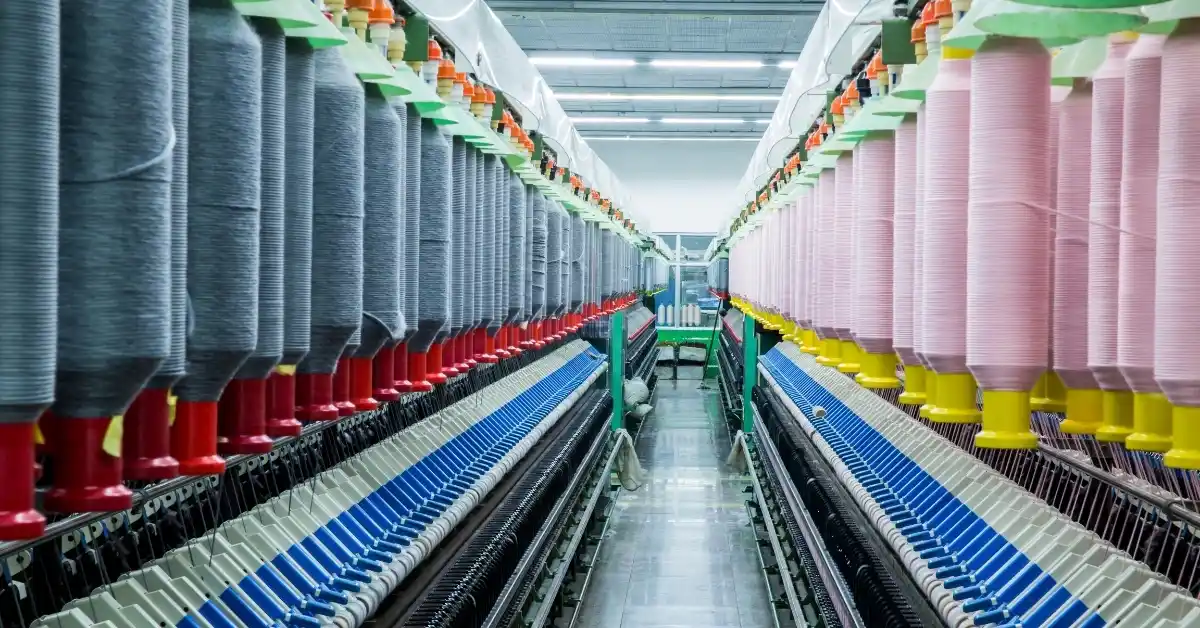 A textile production line featuring rows of yarn spools in various colors, set in a well-lit factory with precision machinery.