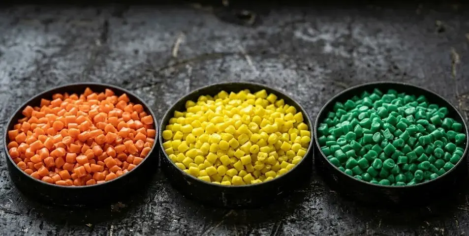 Three colorful silicone pellets in orange, yellow, and green trays on black background, macro industrial material texture, high detail. -Specialty Silicone Materials. -1