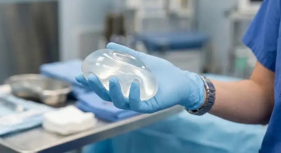 A gloved hand holding a translucent silicone gel implant under soft clinical lighting, medical environment, smooth flexible polymer texture. -What Are Silicones. -1