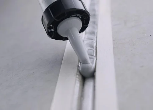 "Applying a smooth bead of waterproof silicone sealant along a bathroom joint using a caulking gun.