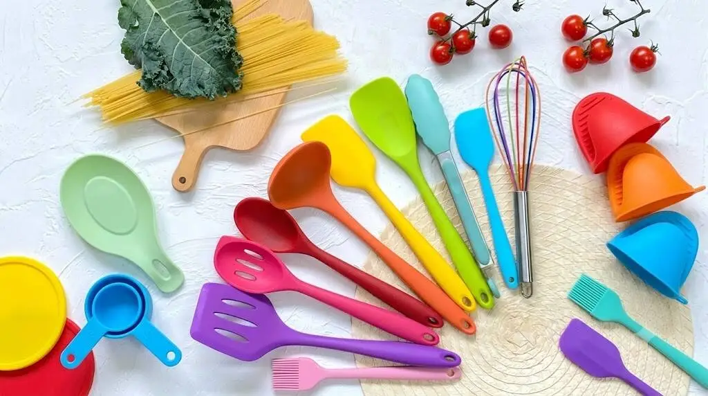 A flat-lay landscape photo showcasing a colorful set of food-grade silicone kitchen utensils neatly arranged on a clean white countertop.