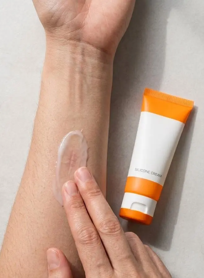 A top-down view of fingertips applying translucent cream on a forearm scar - silicone cream- 2